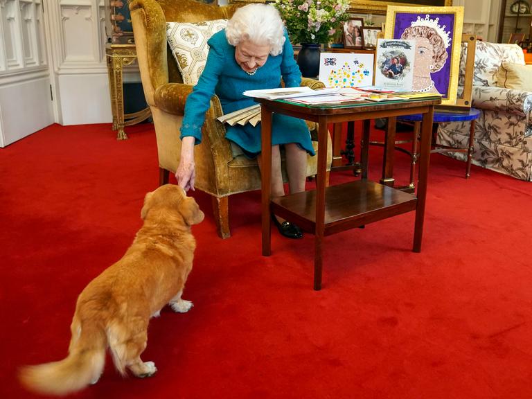 Queen Elizabeth II. sitzt in einem Sessel und streichelt einen ihrer Hunde.