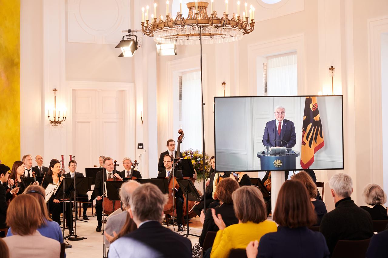 Die Berliner Philharmoniker sitzen im Schloss Bellevue vor ein paar Dutzend Zuschauern während Bundespräsident Frank-Walter Steinmeier wegen Krankheit per Video zugeschaltet ist.

