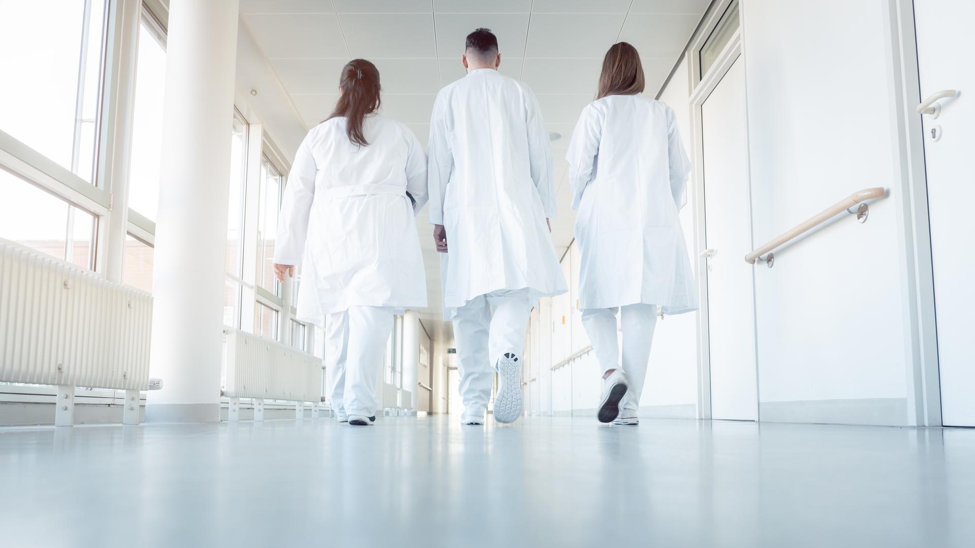 Zwei Ärztinnen und ein Arzt gehen in einem Krankenhausflur. Zwei Ärztinnen und ein Arzt gehen in einem Krankenhausflur.
