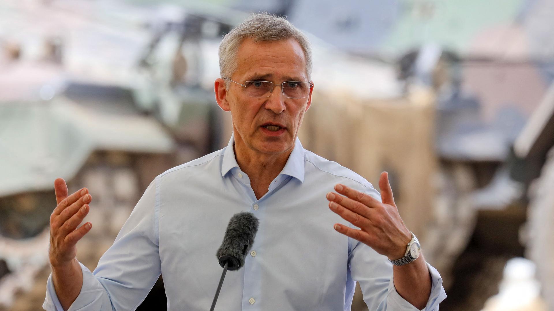 NATO-Generalsekretär Jens Stoltenberg in Zivil mit weißem Hemd in Litauen, im Hintergrund ist militärische Ausrüstung zu sehen