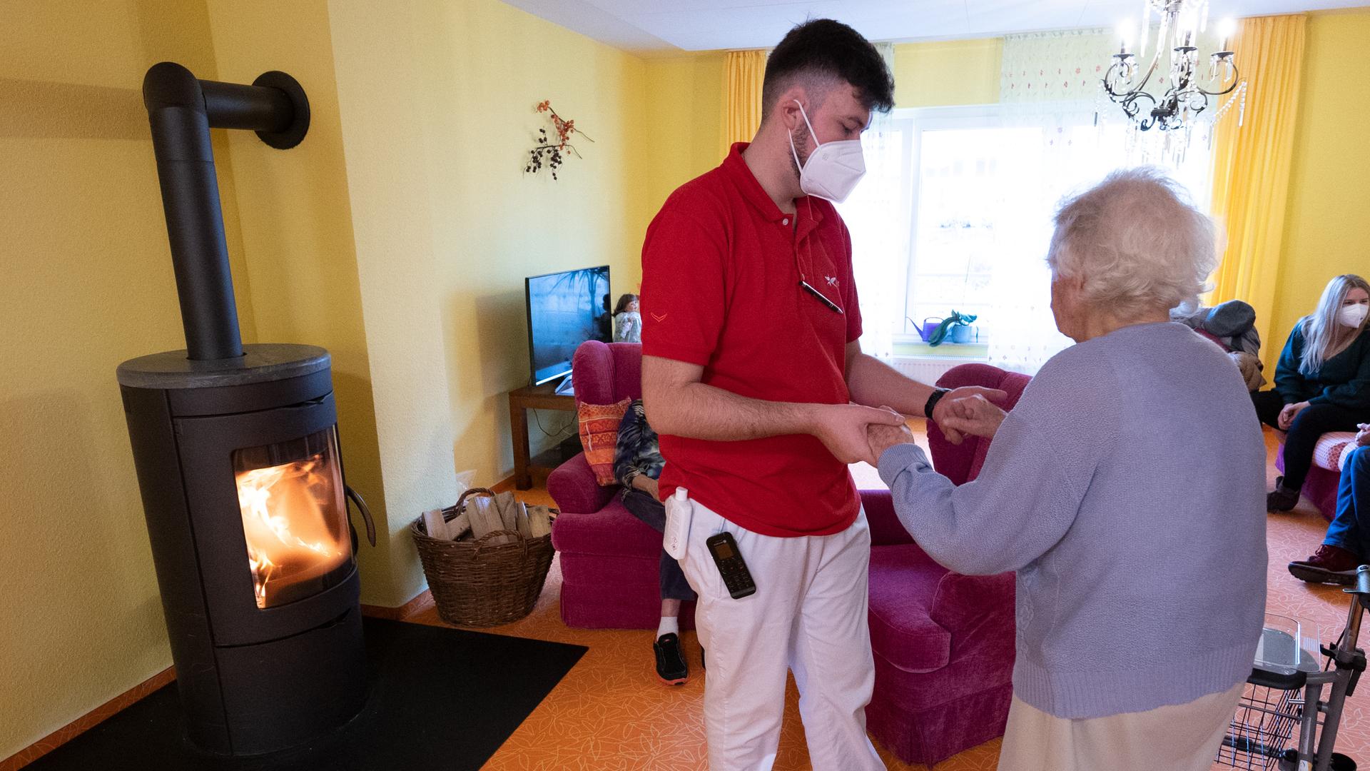 Ein Betreuer hilft im Altenheim einer Bewohnerin in einer Wohngruppe.