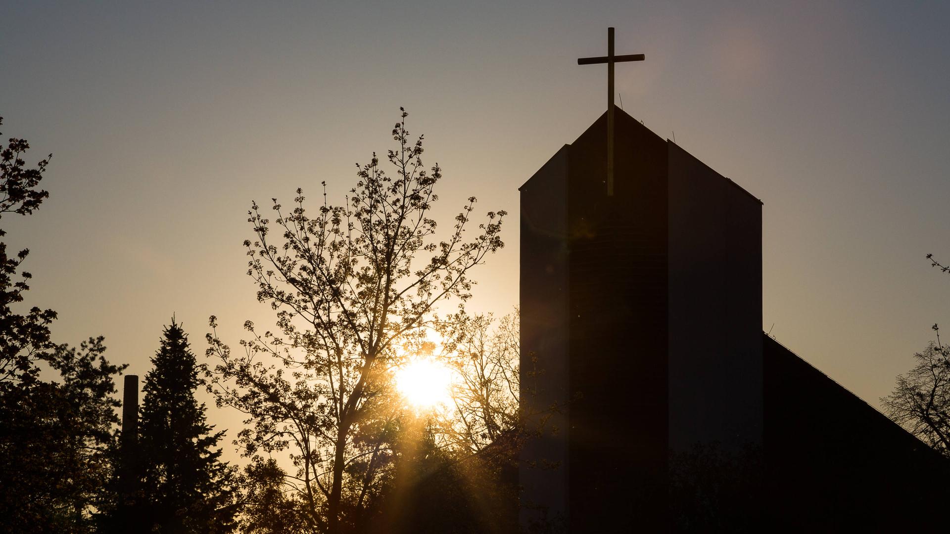 Ein Kirchturm mit Kreuz steht im Gegenlicht der Sonne. Ein Kirchturm mit Kreuz steht im Gegenlicht der Sonne.