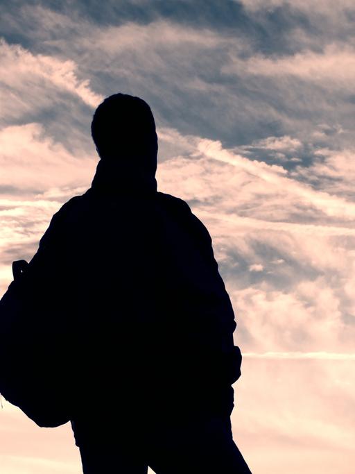 Ein namenloser Mann im Nirgendwo unterwegs. Zu sehen: Ein Mann steht mit dem Rücken zur Kamera und schaut in die Wolken. 
