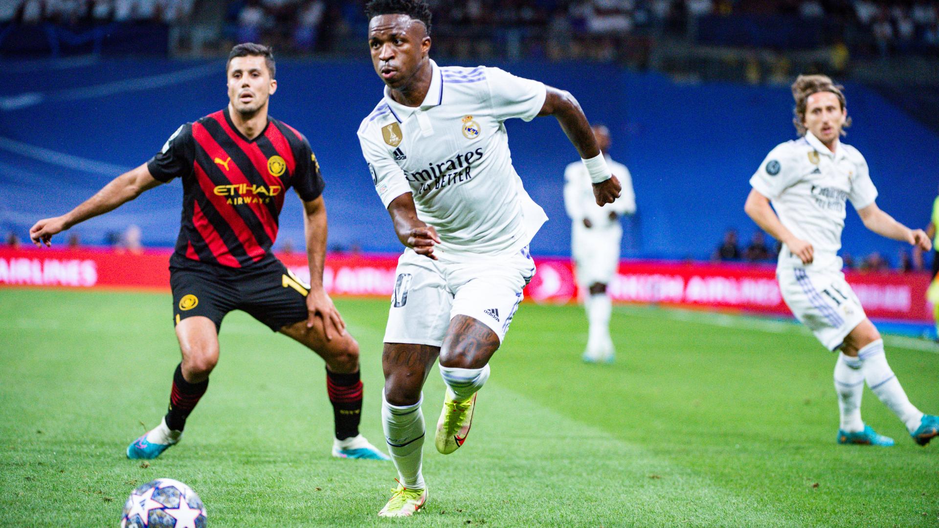 Der Fußball-Spieler mit dem weißen Trikot ist Vinicius Junior. Das Foto zeigt ihn beim Fußball-Spiel. Der Fußball-Spieler mit dem weißen Trikot ist Vinicius Junior. Das Foto zeigt ihn beim Fußball-Spiel.