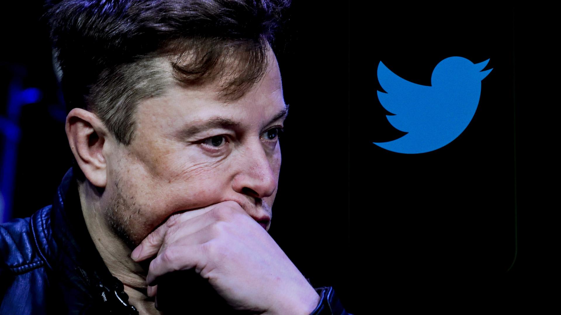 Elon Musk hält seine linke Hand nachdenklich an sein Kinn. Im Hintergrund sieht man das Twitter-Logo. Elon Musk hält seine linke Hand nachdenklich an sein Kinn. Im Hintergrund sieht man das Twitter-Logo.