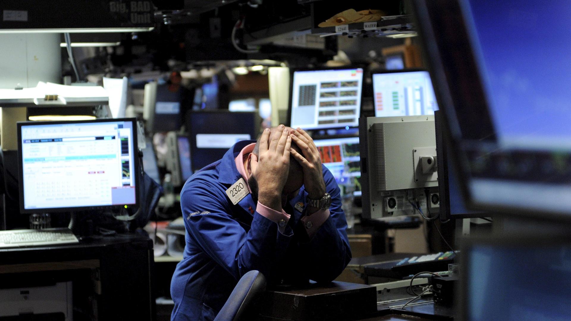 Ein Händler an der Börse, umringt von Monitoren, hält sich aus Verzweiflung den Kopf.