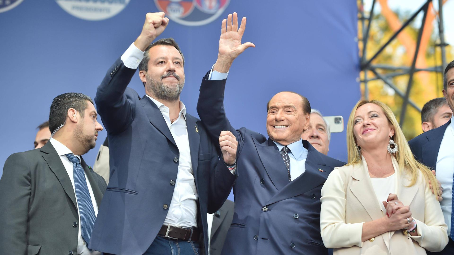 Matteo Salvini und Silvio Berlusconi heben jeweils ihre rechte Hand und stehen links neben Giorgia Meloni. Matteo Salvini und Silvio Berlusconi heben jeweils ihre rechte Hand und stehen links neben Giorgia Meloni.