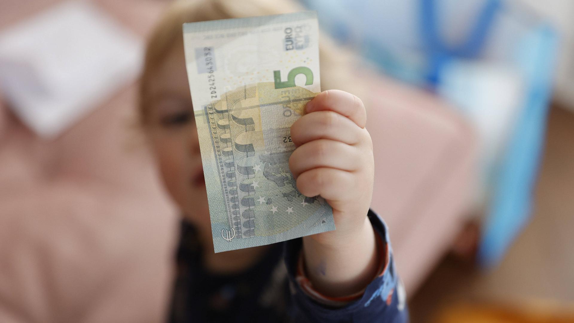 Eine Kinderhand hält einen Fünf-Euro-Schein. Eine Kinderhand hält einen Fünf-Euro-Schein.