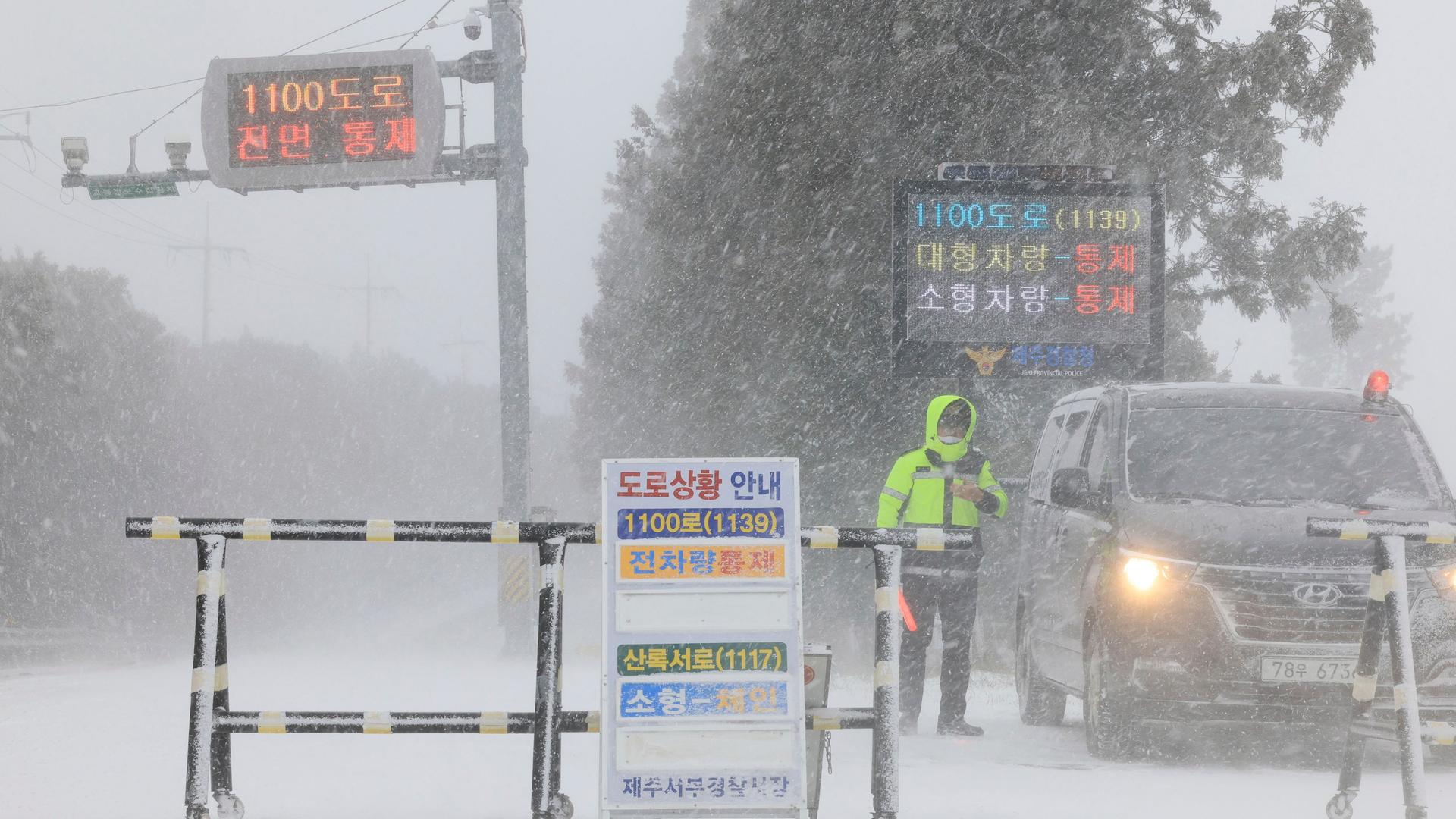 Ein Polizist steht bei Schneefall hinter einer Straßensperre neben einem Fahrzeug. Ein Polizist steht bei Schneefall hinter einer Straßensperre neben einem Fahrzeug.