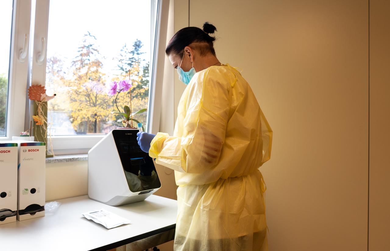 Eine Person in Schutzkleidung steht mit einer Probe in der Hand vor einer "Vivalytic"-Analysemaschinen von Bosch 