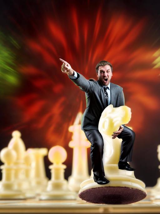 Ein weißer Mann sitzt auf einer weißen Schachfigur auf einem Schachbrett und gibt mit seinem Finger die Richtung vor.
