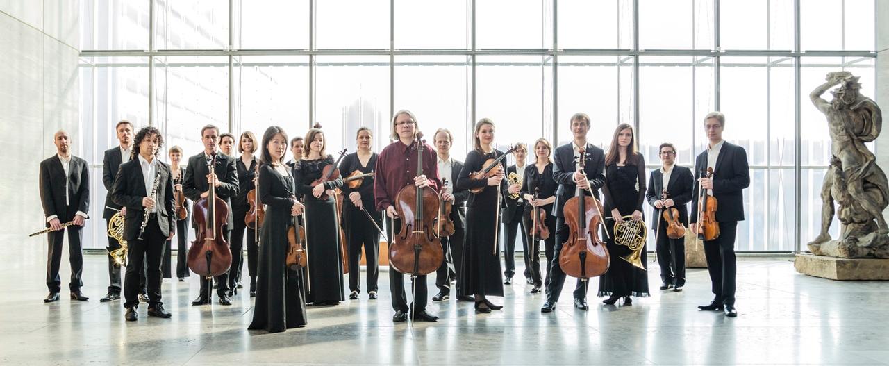 Das Orchdester steht in einem modernen, lichtdurchfluteten Foyer eines Museums. Das Orchdester steht in einem modernen, lichtdurchfluteten Foyer eines Museums.