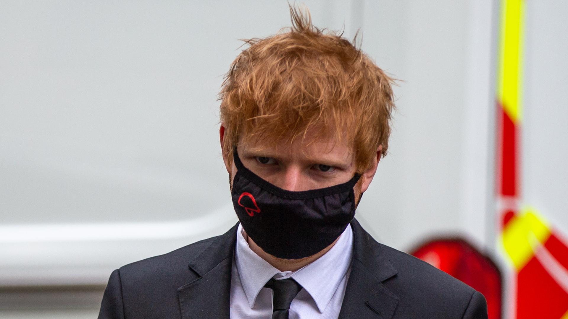 Musiker Ed Sheeran erscheint in Anzug und Krawatte, mit einer Schutzmaske im Gesicht, vor Gericht. Der Musiker hat rote, strubbelige Haare. Musiker Ed Sheeran erscheint in Anzug und Krawatte, mit einer Schutzmaske im Gesicht, vor Gericht. Der Musiker hat rote, strubbelige Haare.