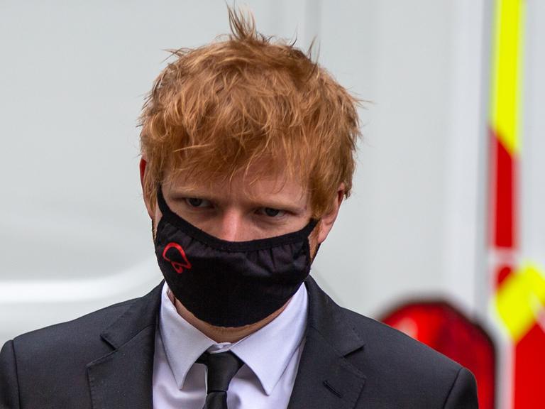 Musiker Ed Sheeran erscheint in Anzug und Krawatte, mit einer Schutzmaske im Gesicht, vor Gericht. Der Musiker hat rote, strubbelige Haare.
