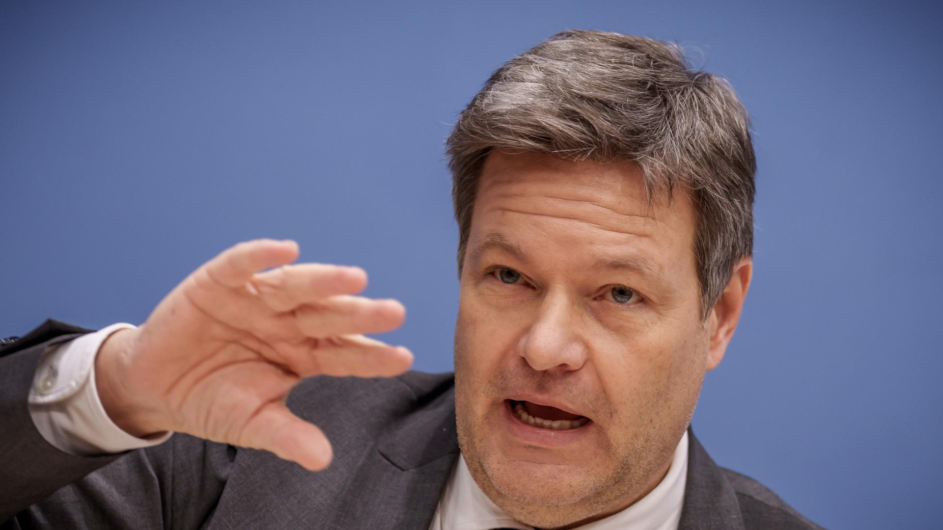 Bundeswirtschaftsminister Habeck im Portrait vor einer blauen Wand. Er hebt die rechte Hand Bundeswirtschaftsminister Habeck im Portrait vor einer blauen Wand. Er hebt die rechte Hand