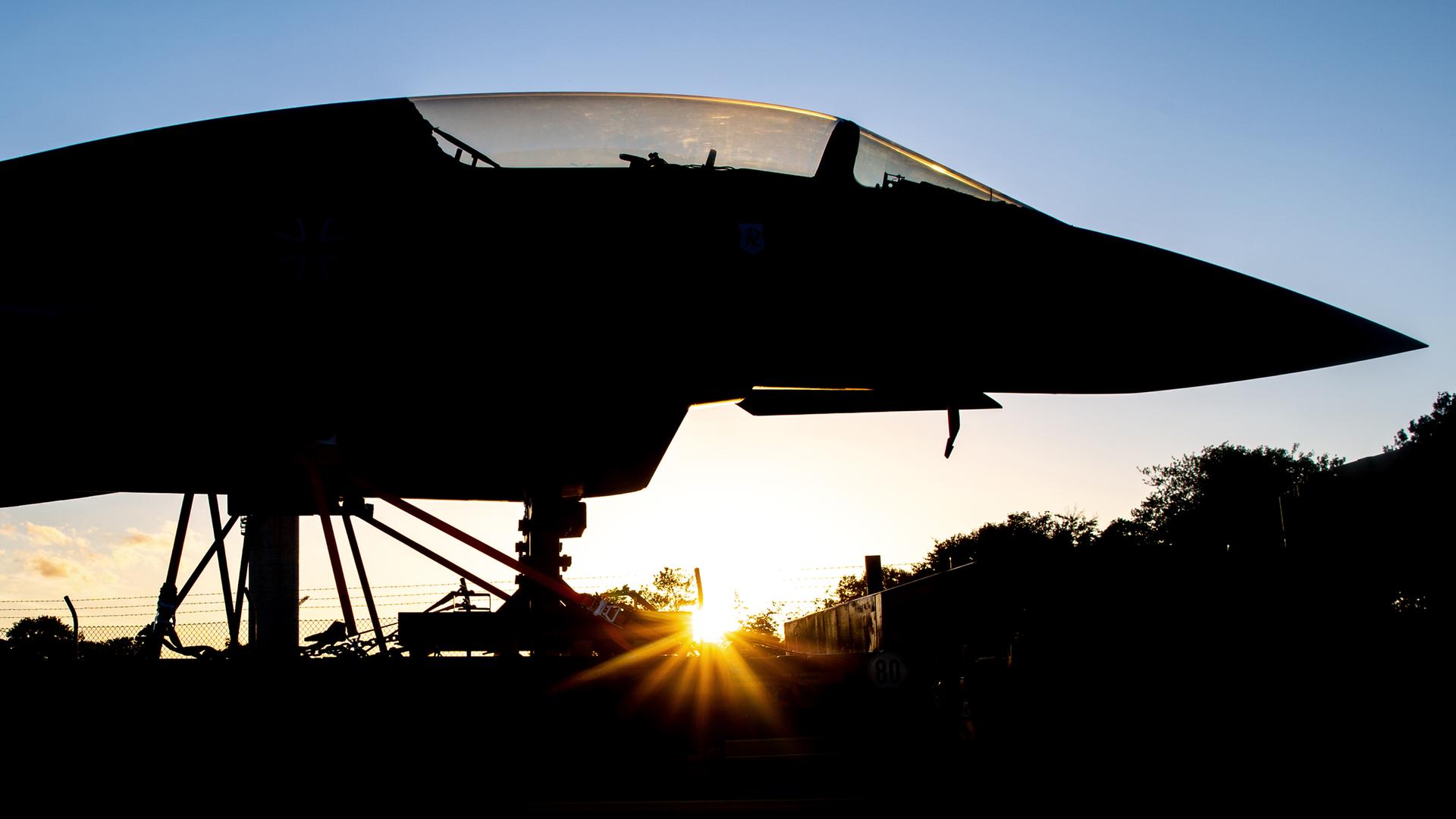 Ein Kampfflugzeug steht im Gegenlicht der Sonne, weshalb es nur in seinen Umrissen zu erkennen ist. 
