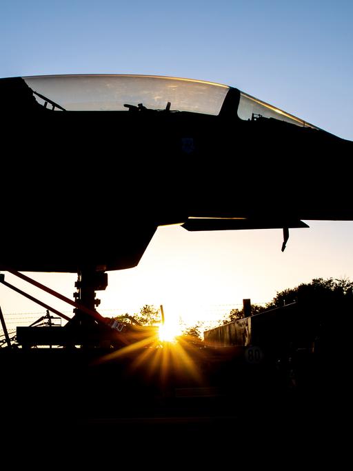 Ein Kampfflugzeug steht im Gegenlicht der Sonne, weshalb es nur in seinen Umrissen zu erkennen ist. 