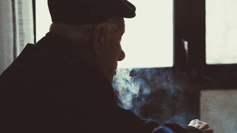 Ein alter Mann von schräg hinten in einem Raum umgeben von Zigarettenrauch