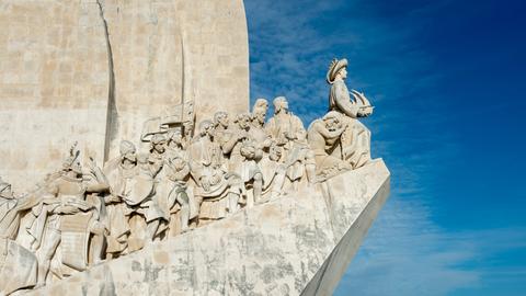 Das Foto zeigt das Denkmal für die Entdeckungen am Ufer des Flusses Tejo in Lissabon. Darauf abgebildet sind u.a. Heinrich der Seefahrer, Vasco da Gama und viele andere koloniale Entdecker. 