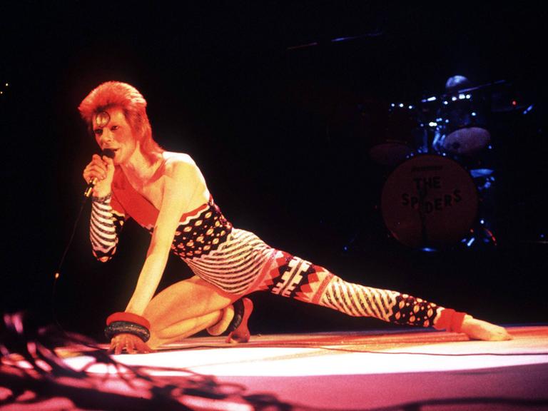 Sänger David Bowie während eines Konzerts in London auf der Bühne, nach vorne gestreckt, knieend.