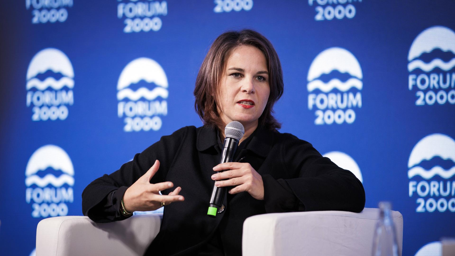 Außenministerin Baerbock hält ein Mikrofon und gestikuliert. Im Hintergrund sieht man das Logo des Forum 2000, das die Podiumsdiskussion in Prag organisiert hat. Außenministerin Baerbock hält ein Mikrofon und gestikuliert. Im Hintergrund sieht man das Logo des Forum 2000, das die Podiumsdiskussion in Prag organisiert hat.