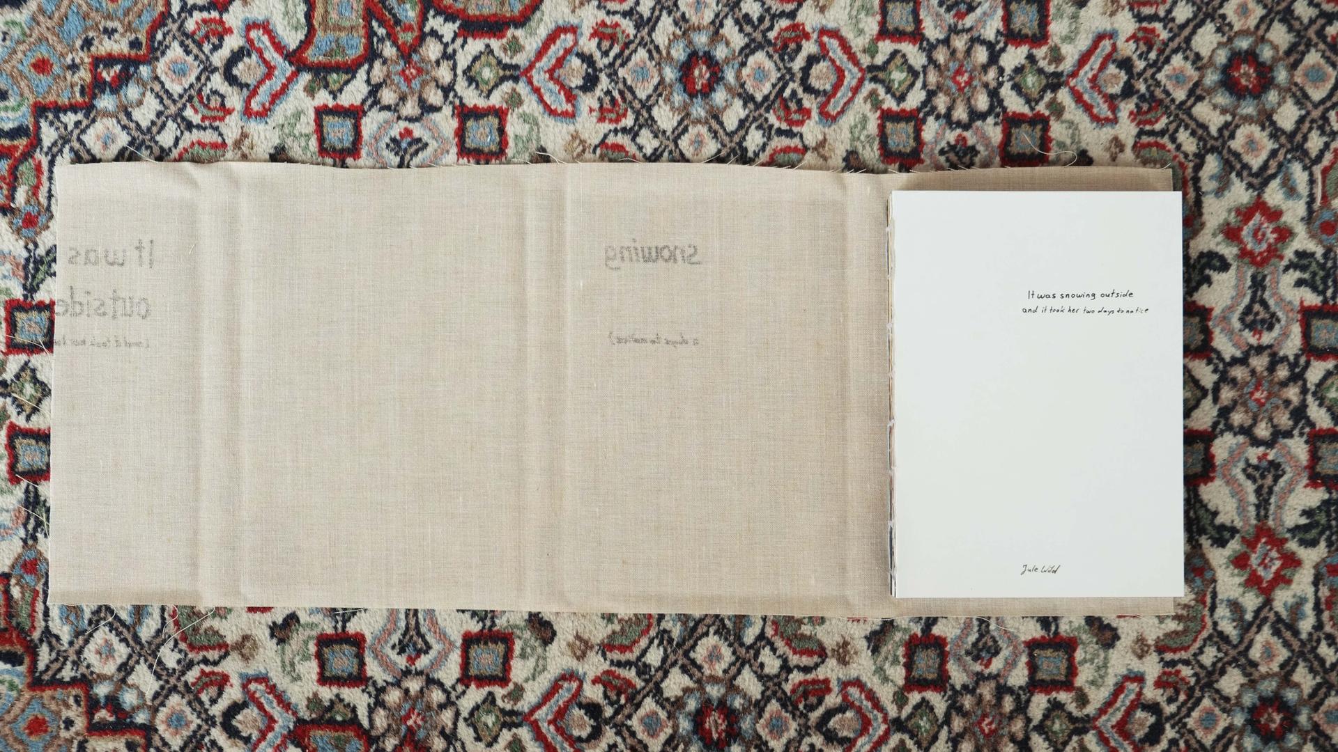 Das Buch liegt auf einem Teppich. Der Umschlag aus ausgefranstem Leinen ist vom gebundenen Buch abgelöst und liegt unter dem Buch auf dem Teppich.