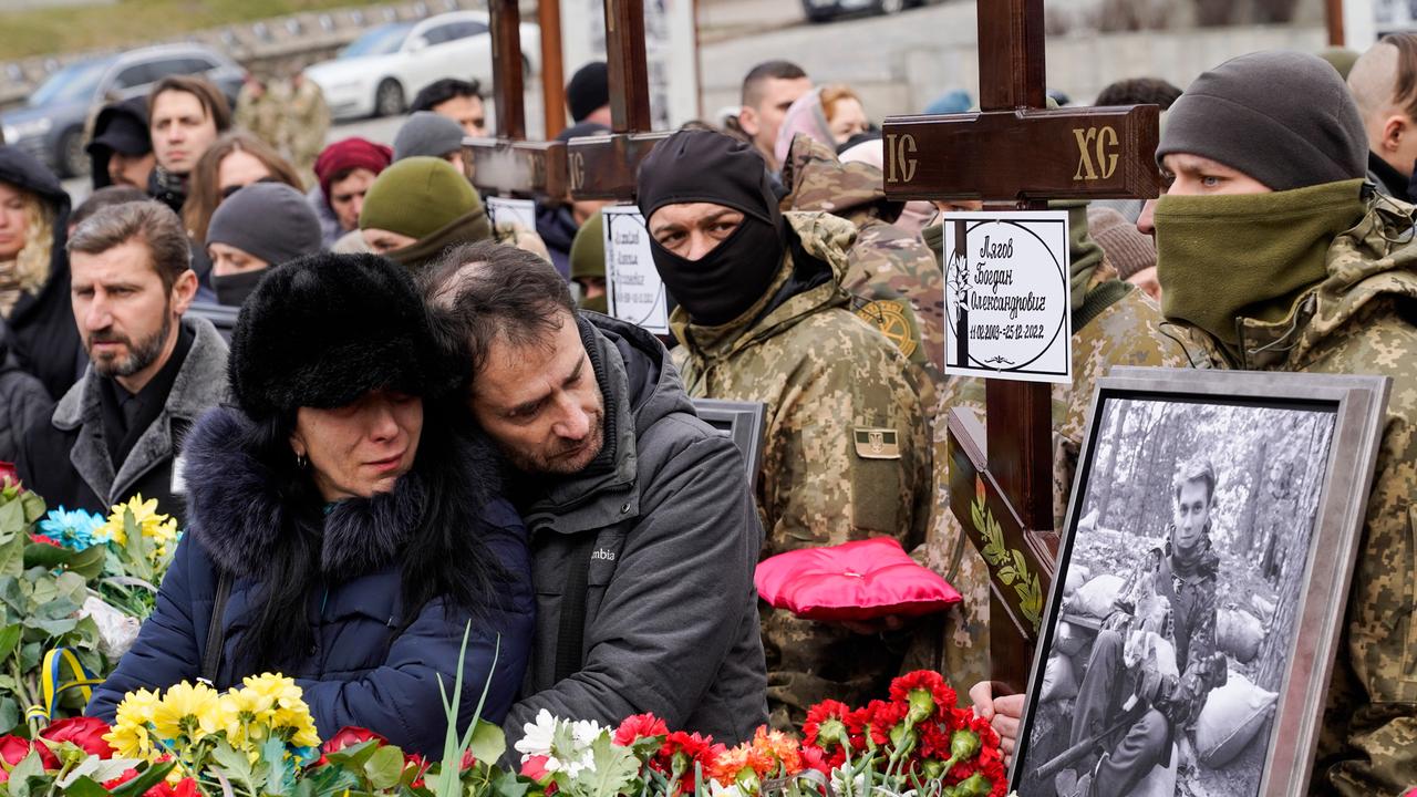 Zivilisten und Soldaten betrauern bei einer Beisetzung Verstorbene auf einem Friedhof.