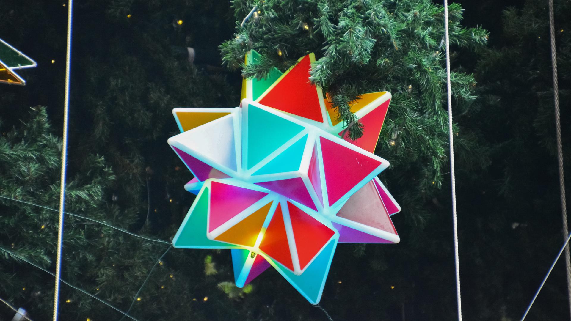 Ein großer, bunter Polyeder hängt an einem geschmückten Tannenbaum. Ein großer, bunter Polyeder hängt an einem geschmückten Tannenbaum.