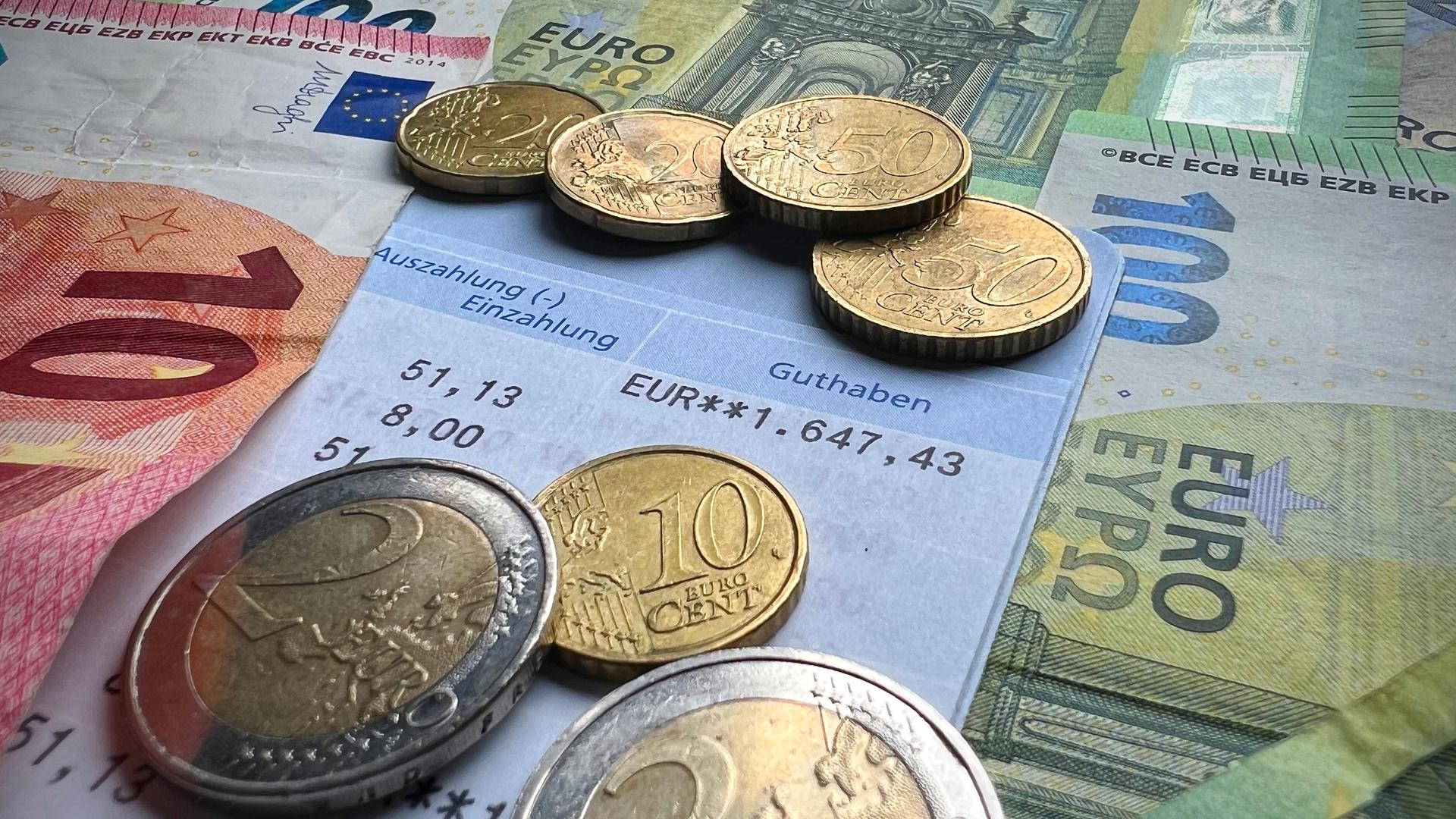 Geldmünzen und Scheine liegen auf einem Sparbuch Geldmünzen und Scheine liegen auf einem Sparbuch