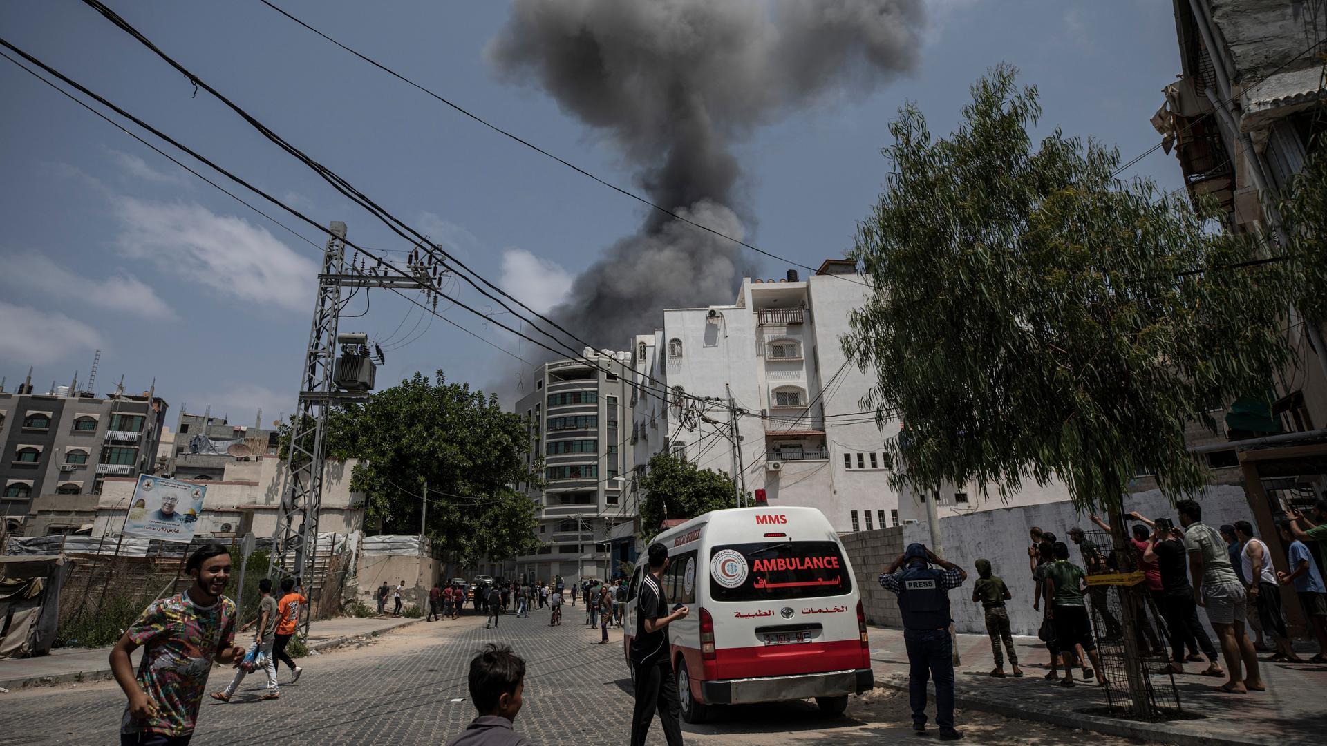 Aus einem Gebäude steigt Rauch auf, im Vordergrund sind Menschen und ein Krankenwagenzu sehen