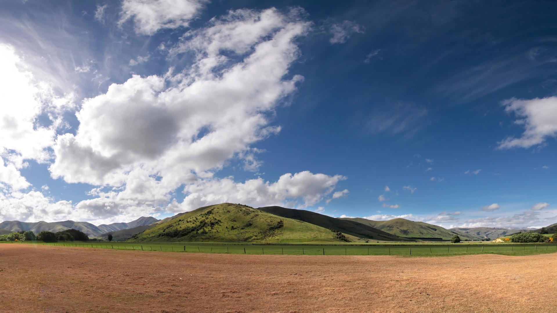 Eine Landschaft in Neuseeland: hinter Bergen türmen sich Wolken auf.