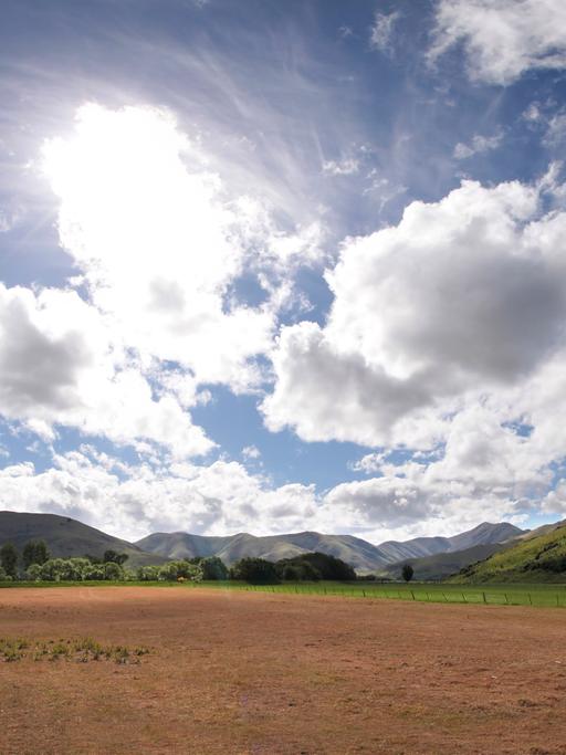 Eine Landschaft in Neuseeland: hinter Bergen türmen sich Wolken auf.
