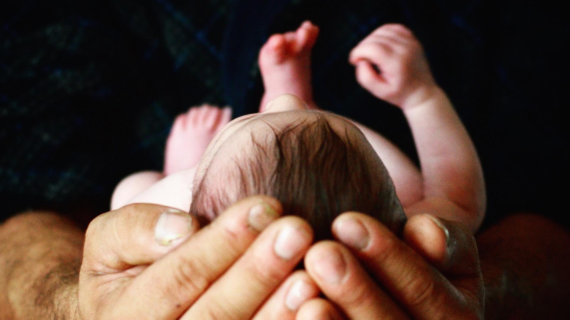 Ein Mann hält sacht einen Kinderkopf in seinen Händen. Ein Mann hält sacht einen Kinderkopf in seinen Händen.