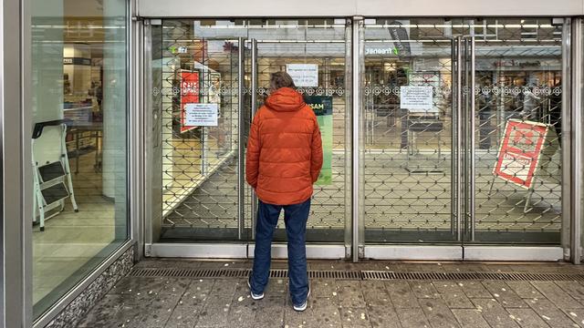 Ein Mann in oranger Jacke steht vor einer geschlossenen Filiale von Galeria Karstadt Kaufhof. 