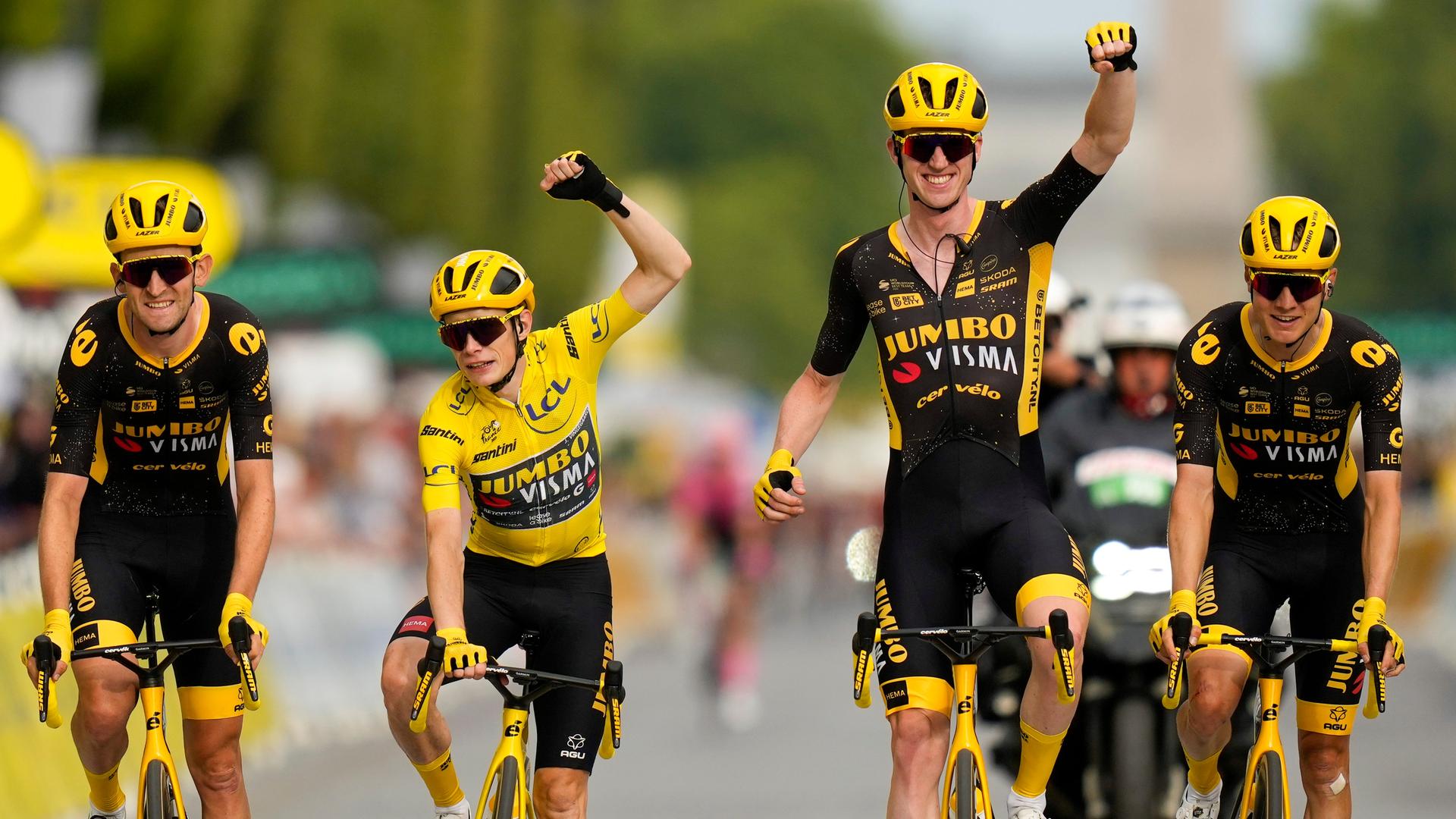 Jonas Vingegaard im gelben Trikot reißt einen Arm hoch und macht eine Faust. Neben ihm sind andere Radfahrer seines Teams.