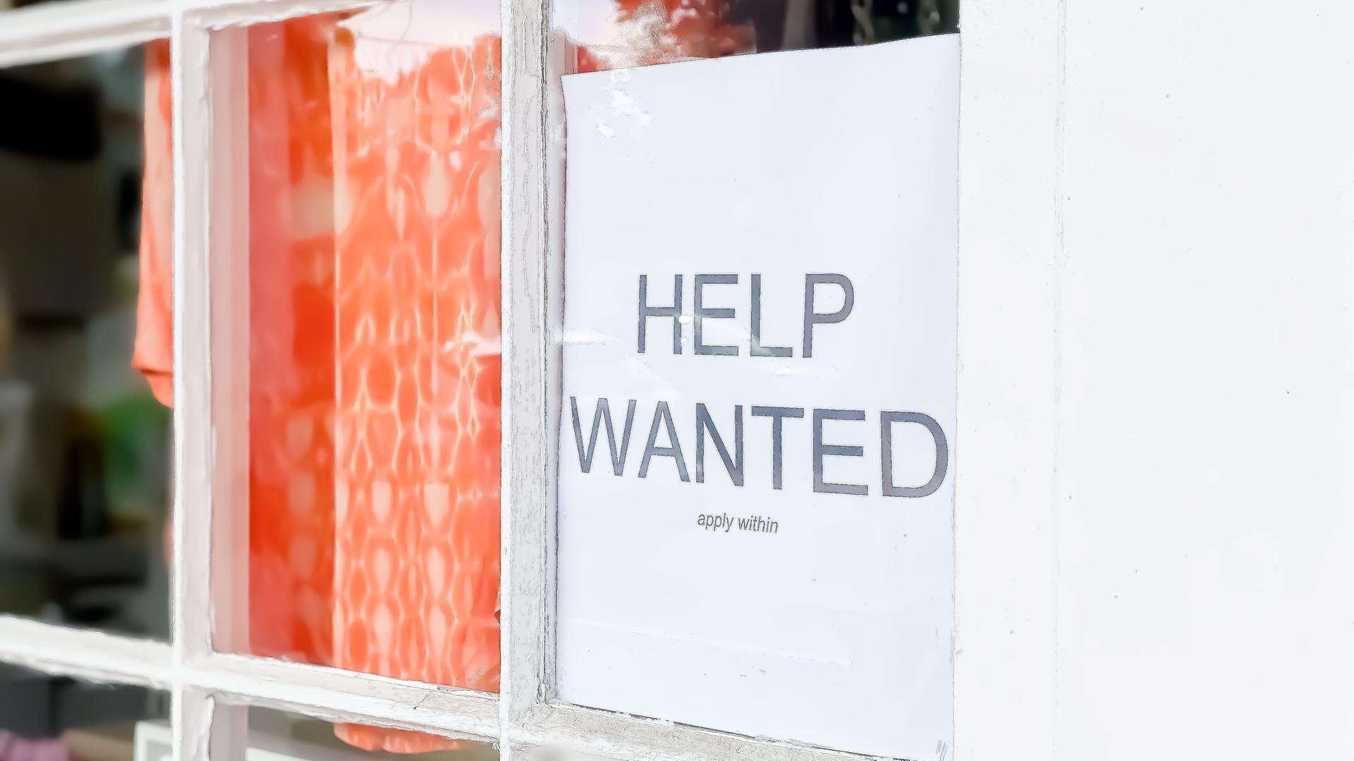 Ein Schild mit der Aufschrift "Help Wanted" hängt im Fenster eines Geschäfts. Ein Schild mit der Aufschrift "Help Wanted" hängt im Fenster eines Geschäfts.
