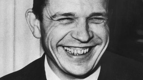 Ein junger Mann auf einer Schwarz-Weiß-Aufnahme: Es ist der Dramatiker Peter Hacks. Er lacht, dabei kommen seine Zähne zum Vorschein, die Augen sind zusammen gekniffen.