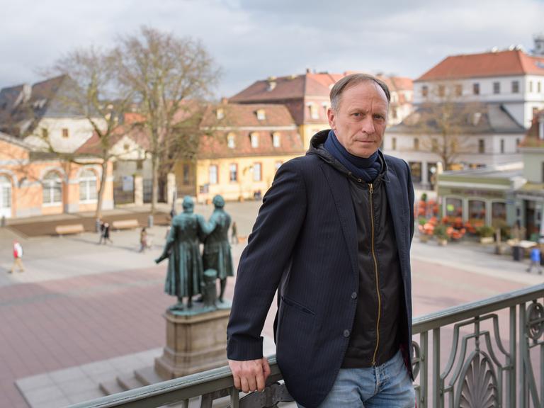 Ein Mann mittleren Alters steht am 07.03.2017 auf dem Balkong des Deutschen Nationaltheater in Weimar (Thüringen), im Hintergrund ein Denkmal von Goethe und Schiller