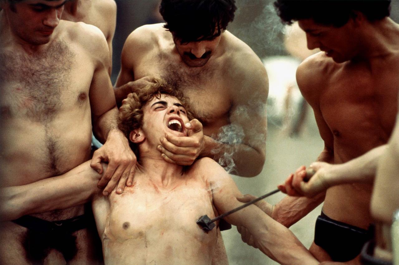 In der Szene aus "Die 100 Tage von Sodom" halten drei Männer einen weiteren jungen Mann fest und verbrennen ihn mit einem Brandzeichen die Brustwarze.