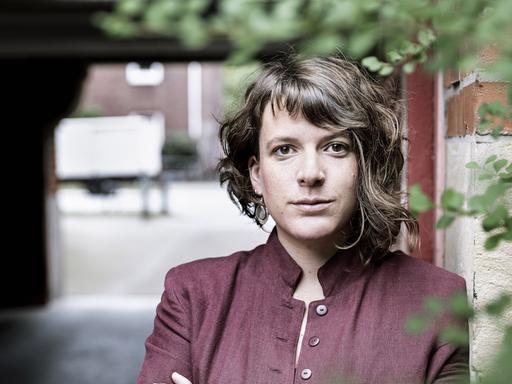 Porträt der Schriftstellerin Laura Cwiertnia, die mit verschränkten Armen an einer Backsteinwand lehnt