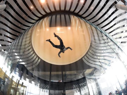 Ein Mensch fliegt oben in einer großen Glaskugel im Windkanal.