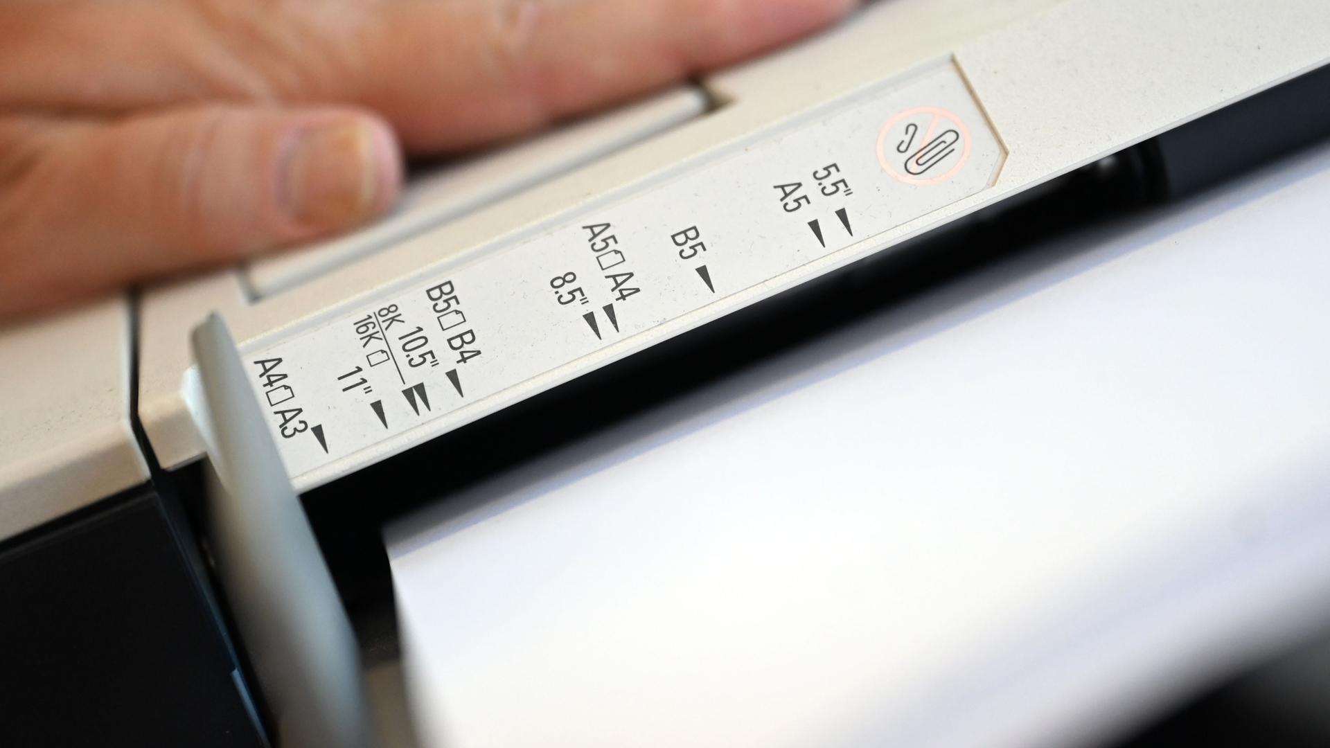 In einer Druckerei sind am Papiereinschub an einem Drucker verschiedene Papierformate angebracht.