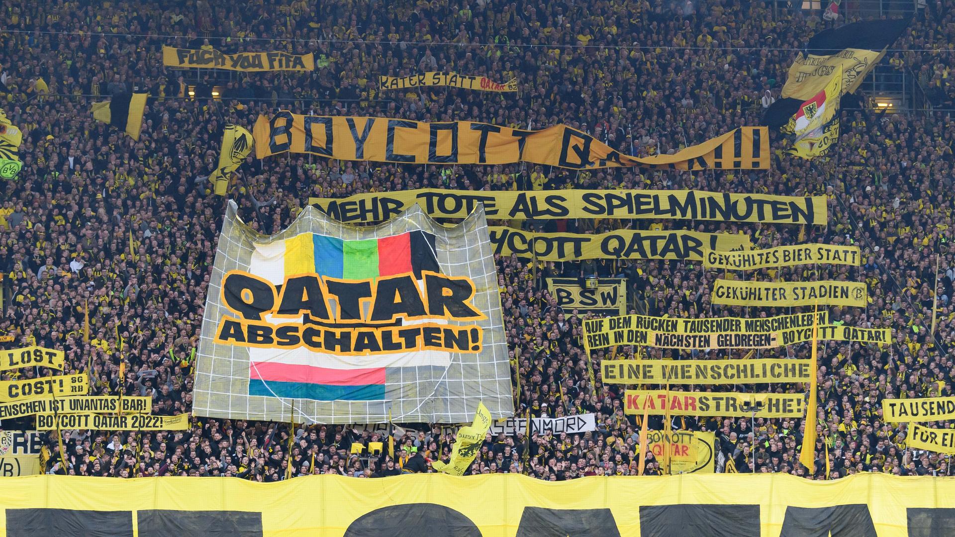 Fans des BVB Dortmund  protestieren auf der Tribüne des Fußballstadions gegen die WM in Katar, Ende November bis Mitte Dezember 2022. Sie haben Transparente entrollt. Eines zeigt das Pausenbild eines Fernsehers mit der Aufforderung "Abschalten".