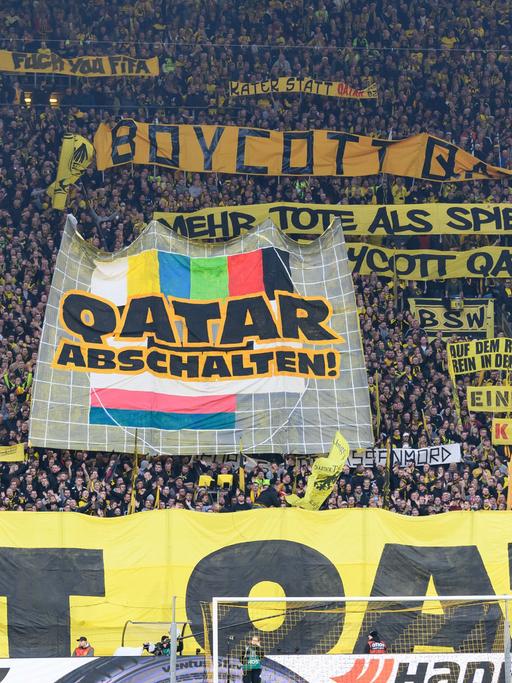 Fans des BVB Dortmund  protestieren auf der Tribüne des Fußballstadions gegen die WM in Katar, Ende November bis Mitte Dezember 2022. Sie haben Transparente entrollt. Eines zeigt das Pausenbild eines Fernsehers mit der Aufforderung "Abschalten".