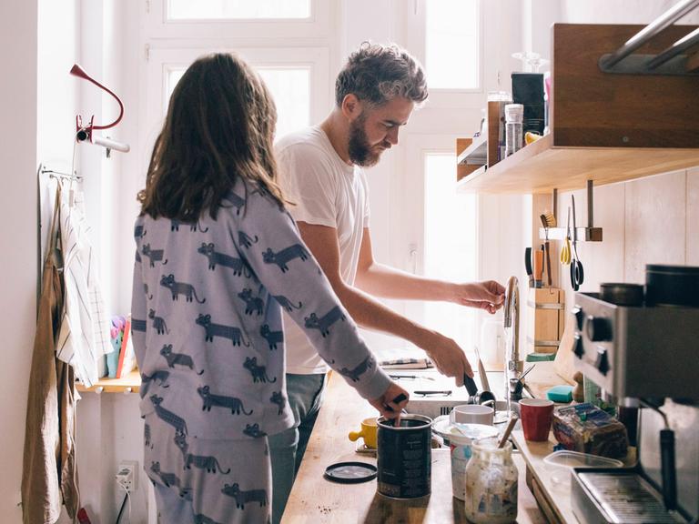 Ein Mann und eine Frau, noch in Schlaganzügen gekleidet, waschen gemeinsam in der Küche ab.