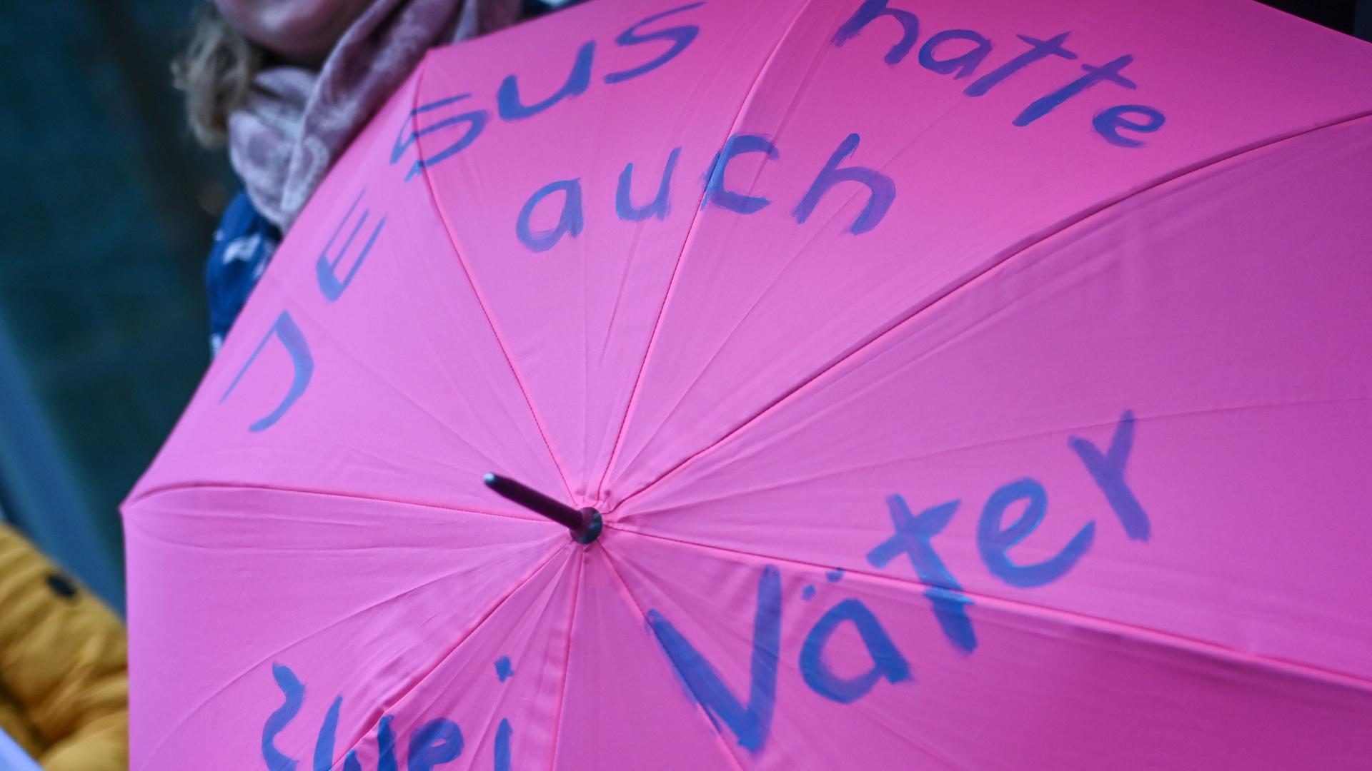 Eine Frau hält bei Protesten am Rande der Synodalversammlung einen Regenschirm mit der Aufschrift "Jesus hatte auch zwei Väter". Eine Frau hält bei Protesten am Rande der Synodalversammlung einen Regenschirm mit der Aufschrift "Jesus hatte auch zwei Väter".