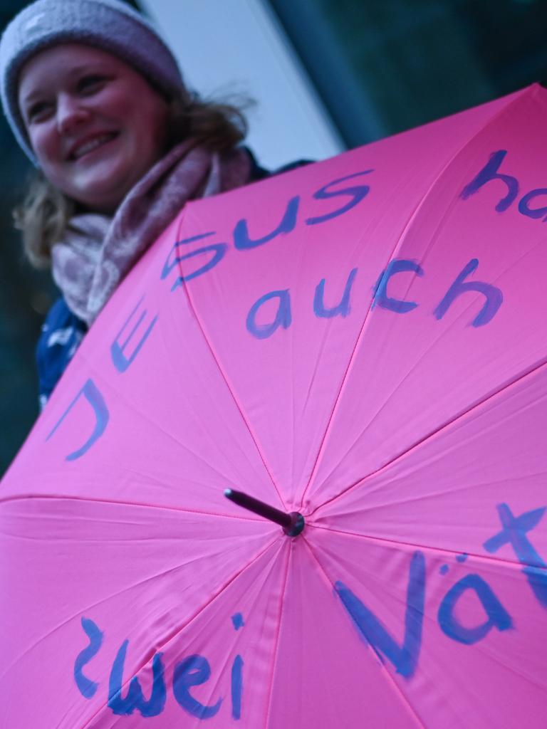 Eine Frau hält bei Protesten am Rande der Synodalversammlung einen Regenschirm mit der Aufschrift "Jesus hatte auch zwei Väter". 