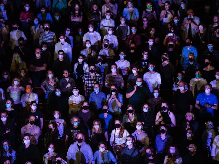 Zuschauer verfolgen stehend ein Konzert in der Kölner Philharmonie. Sie tragen Masken gegen das Coronavirus.