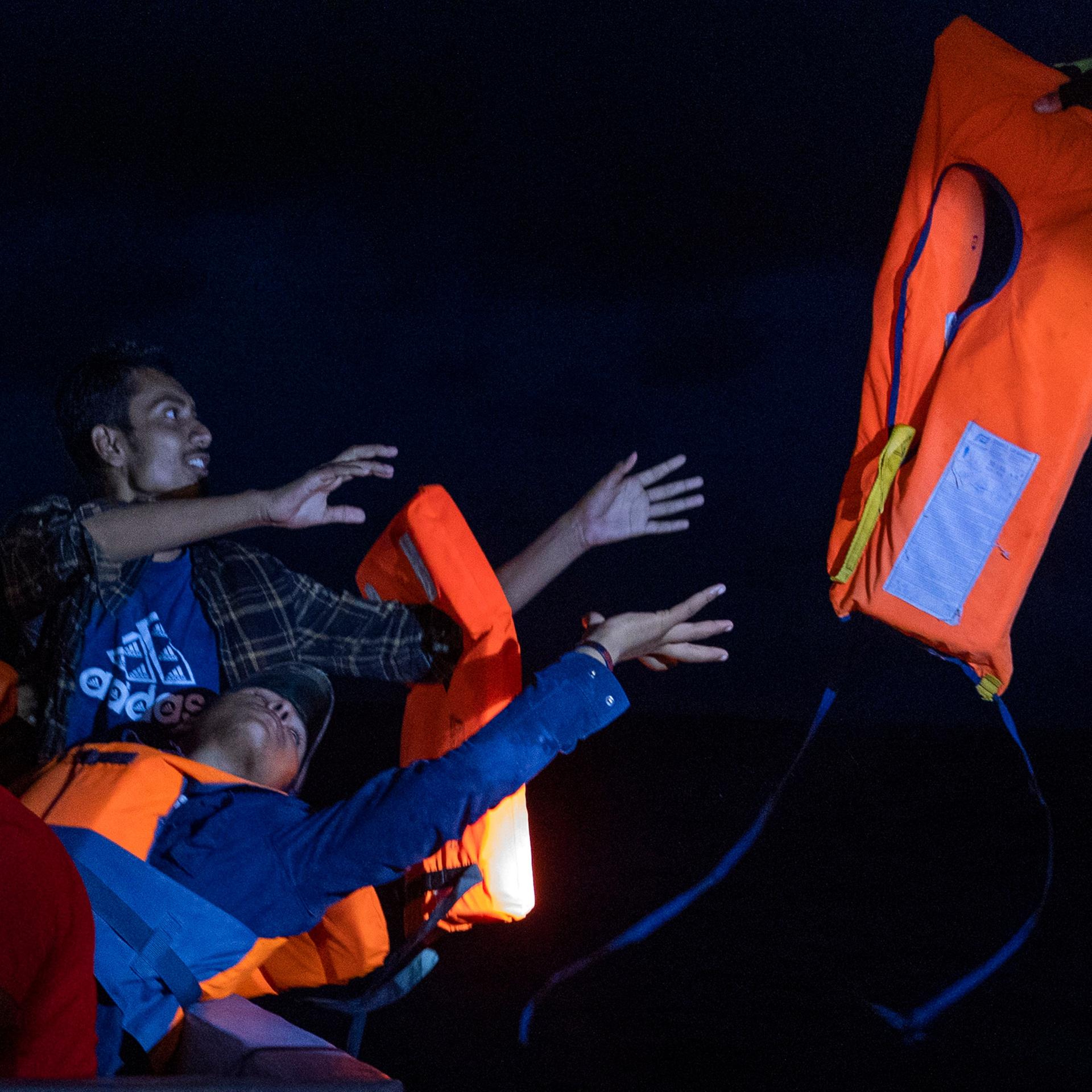 Eine Gruppe von Migranten wird von Freiwilligen des Rettungsschiffs Ocean Viking gerettet. Sie recken die Arme nach einer Schwimmweste. 