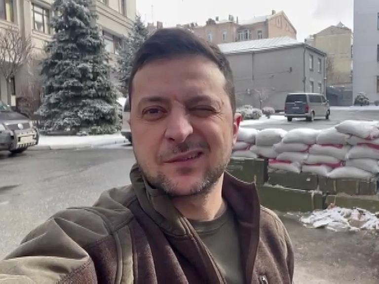 Selfie von Wolodymyr Selenskyj, der in khakifarbener Jacke in einer Straße in Kiew steht und in die Kamera zwinkert.